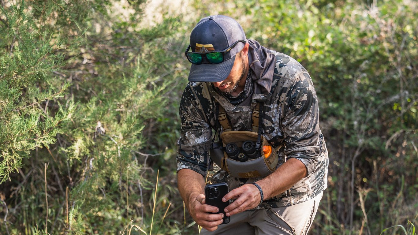 Hunter in camo scanning whitetail antlers with his phone in the brush
