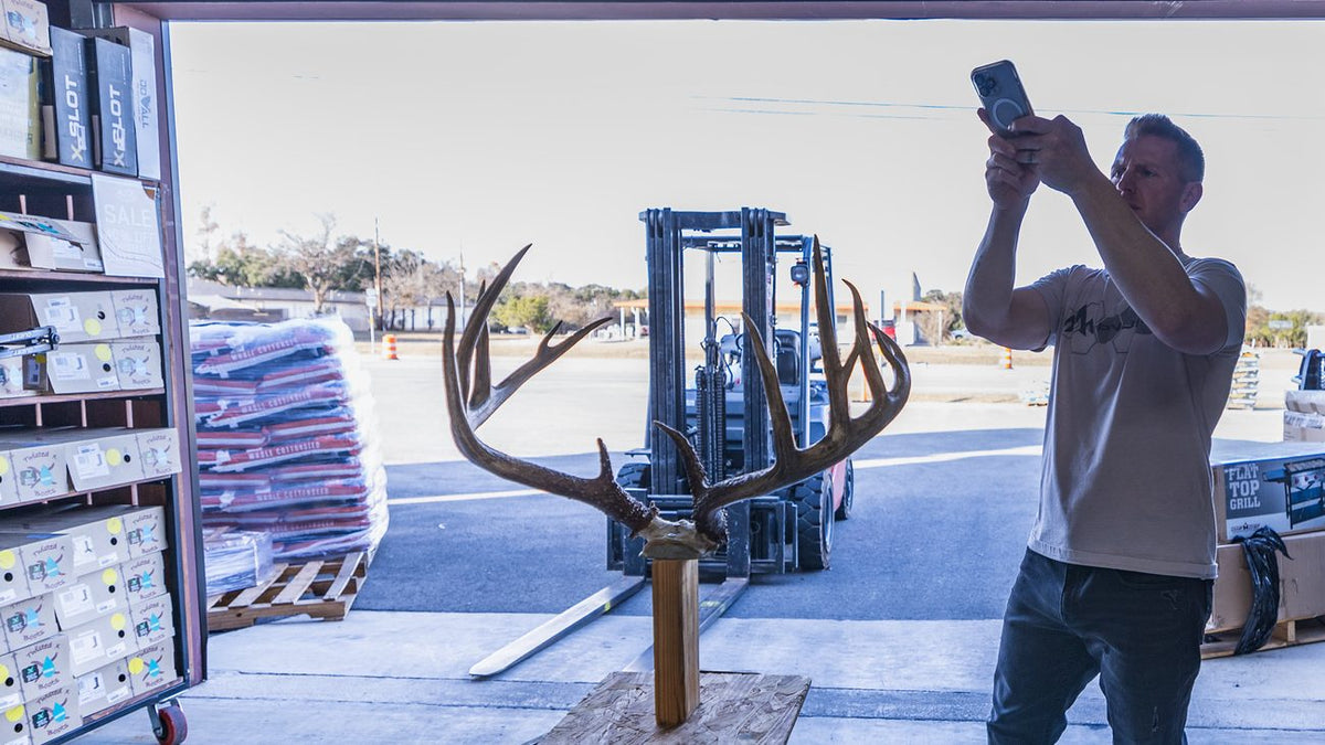 Hunter scanning whitetail antlers on a stand with his phone outside a shop